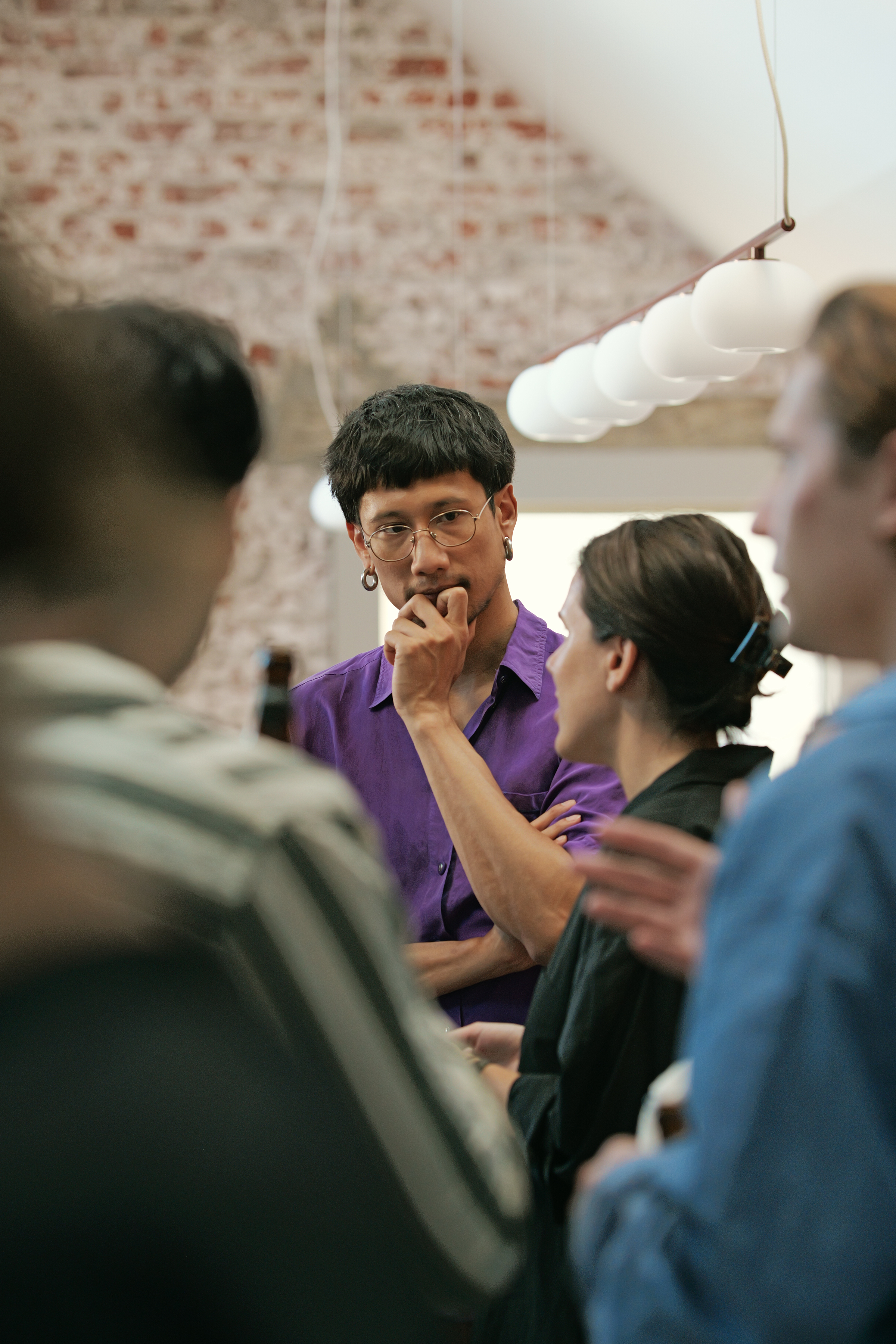 Person in a purple shirt with glasses listening thoughtfully during a conversation in a modern interior setting.