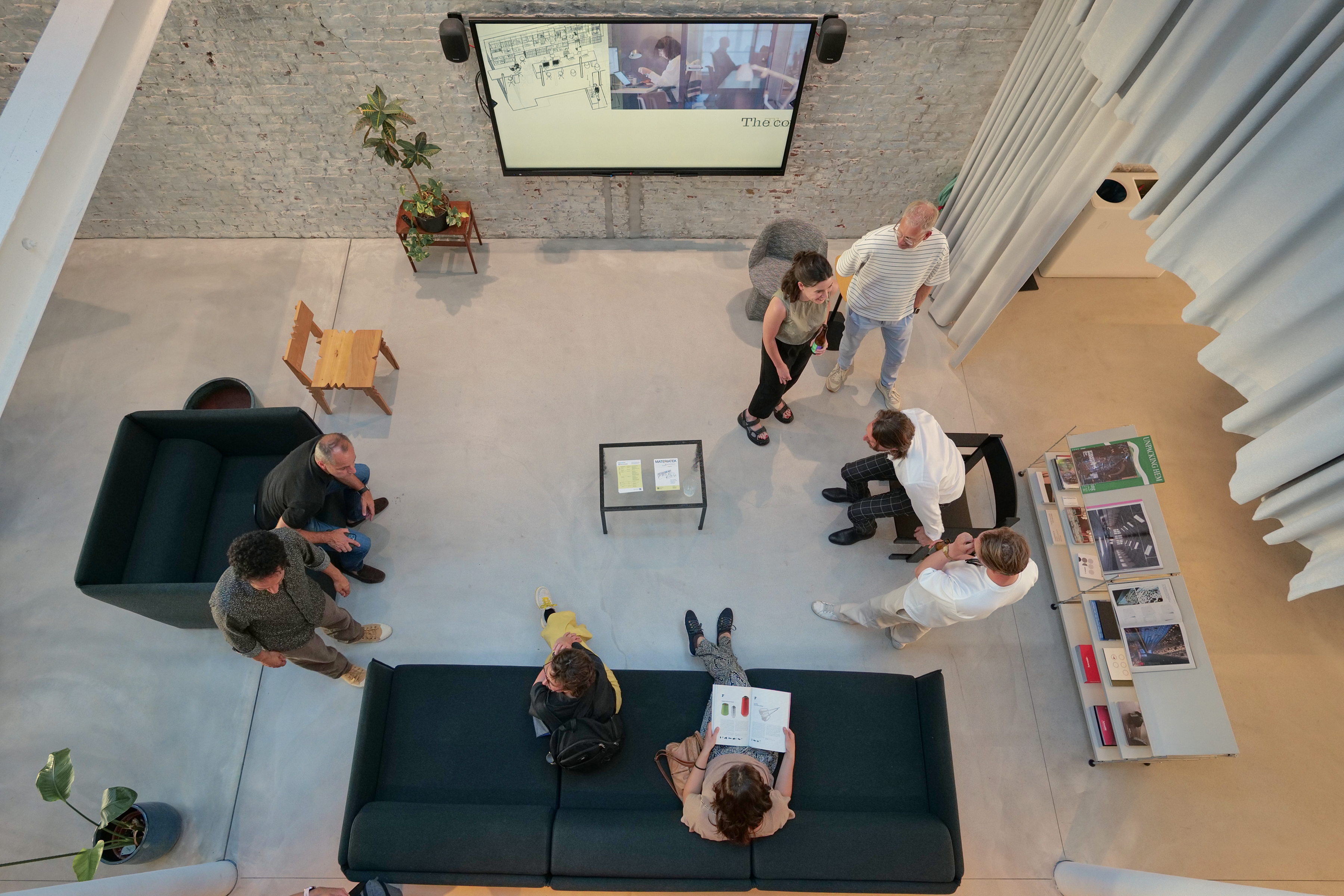 Top view of a group of people gathered in a modern space with sofas, a low table, a projection screen, and a shelf with design books.