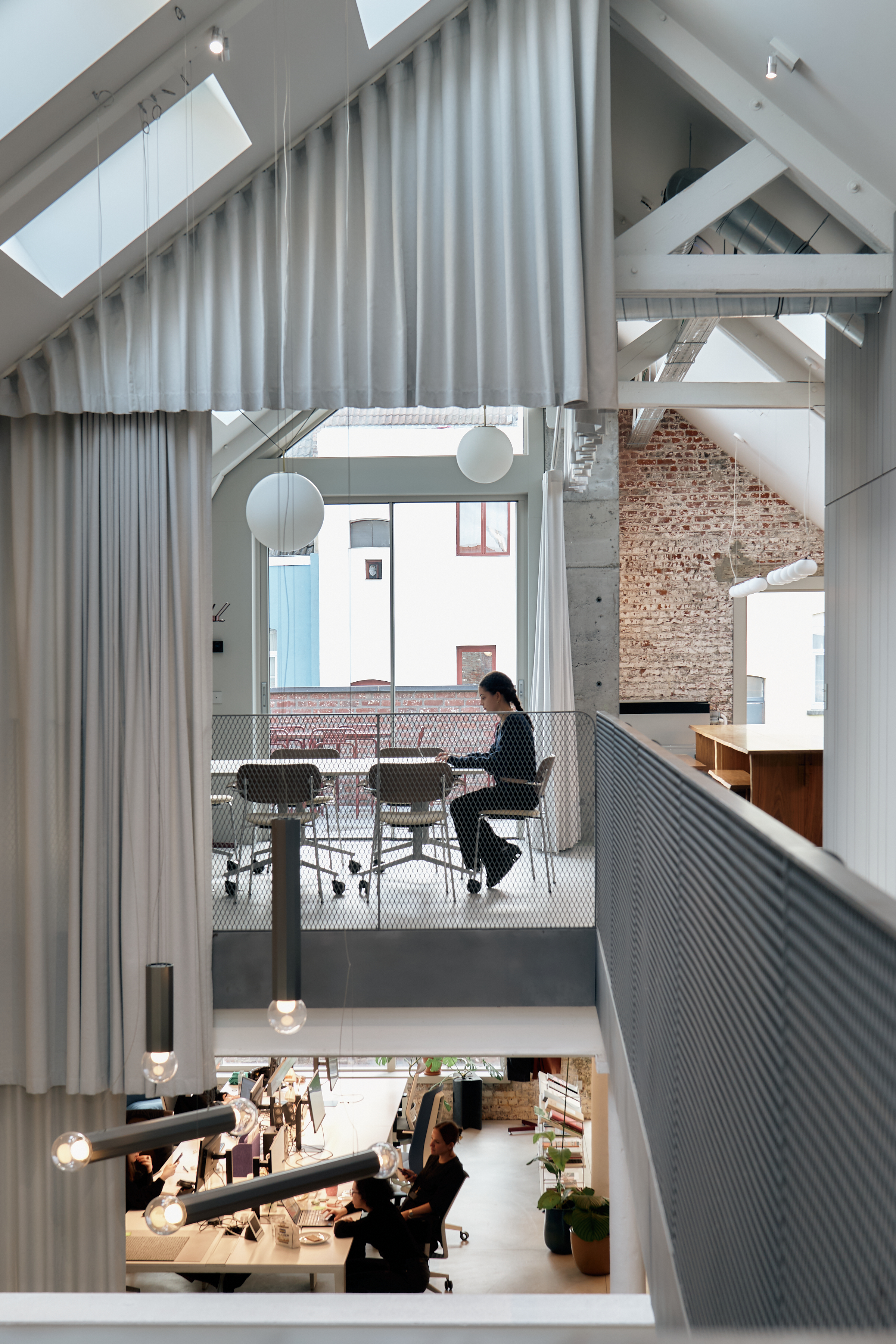 Two-level modern office with exposed beams, skylights, and a person working in the upper meeting area.