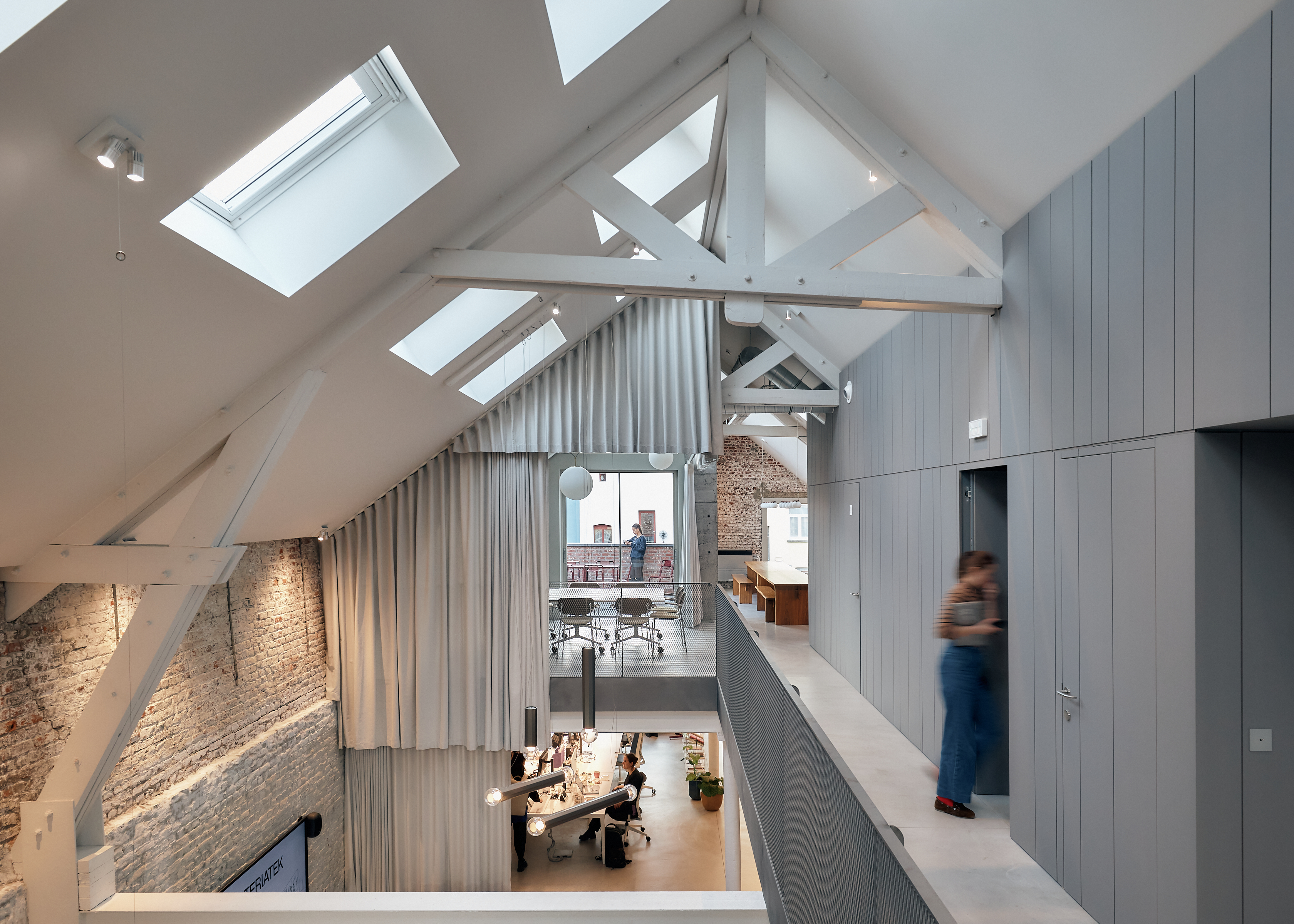 Modern office mezzanine with exposed beams, skylights, and long hallway overlooking the workspace below.