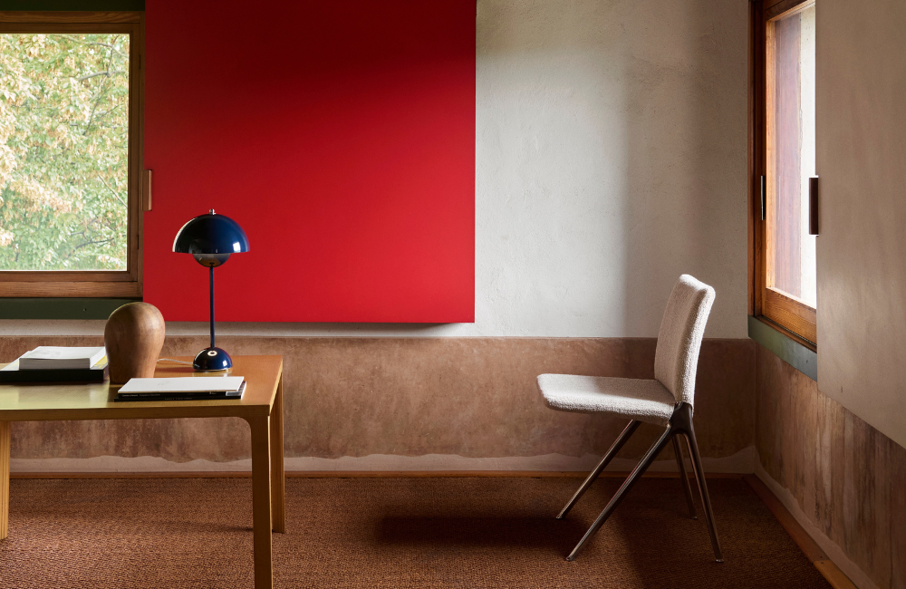 Minimal interior with wooden desk, blue table lamp and upholstered chair set against a red wall and natural light at Materiatek